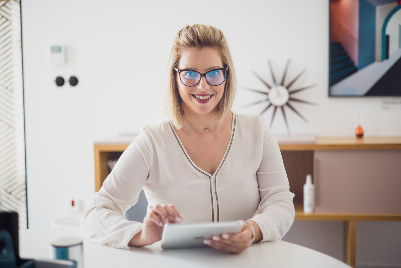 Andrea Čerina, the business owner, smiling at the camera while holding a tablet at her desk.